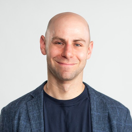 A bald man smiling in front of a white background.
