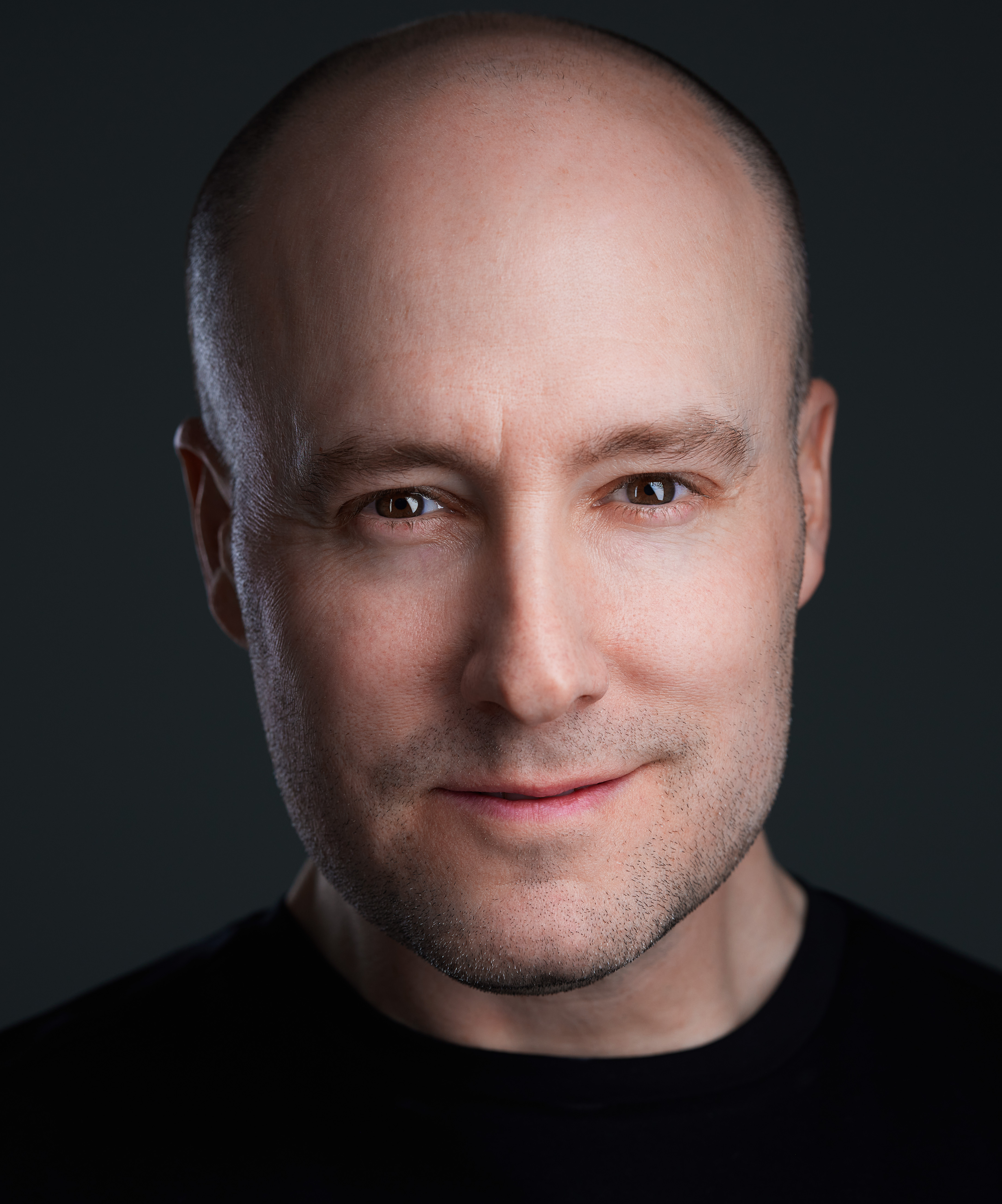 A bald man in a black shirt is posing for a photo.