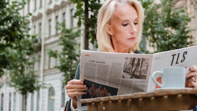 A woman reads a newspaper.