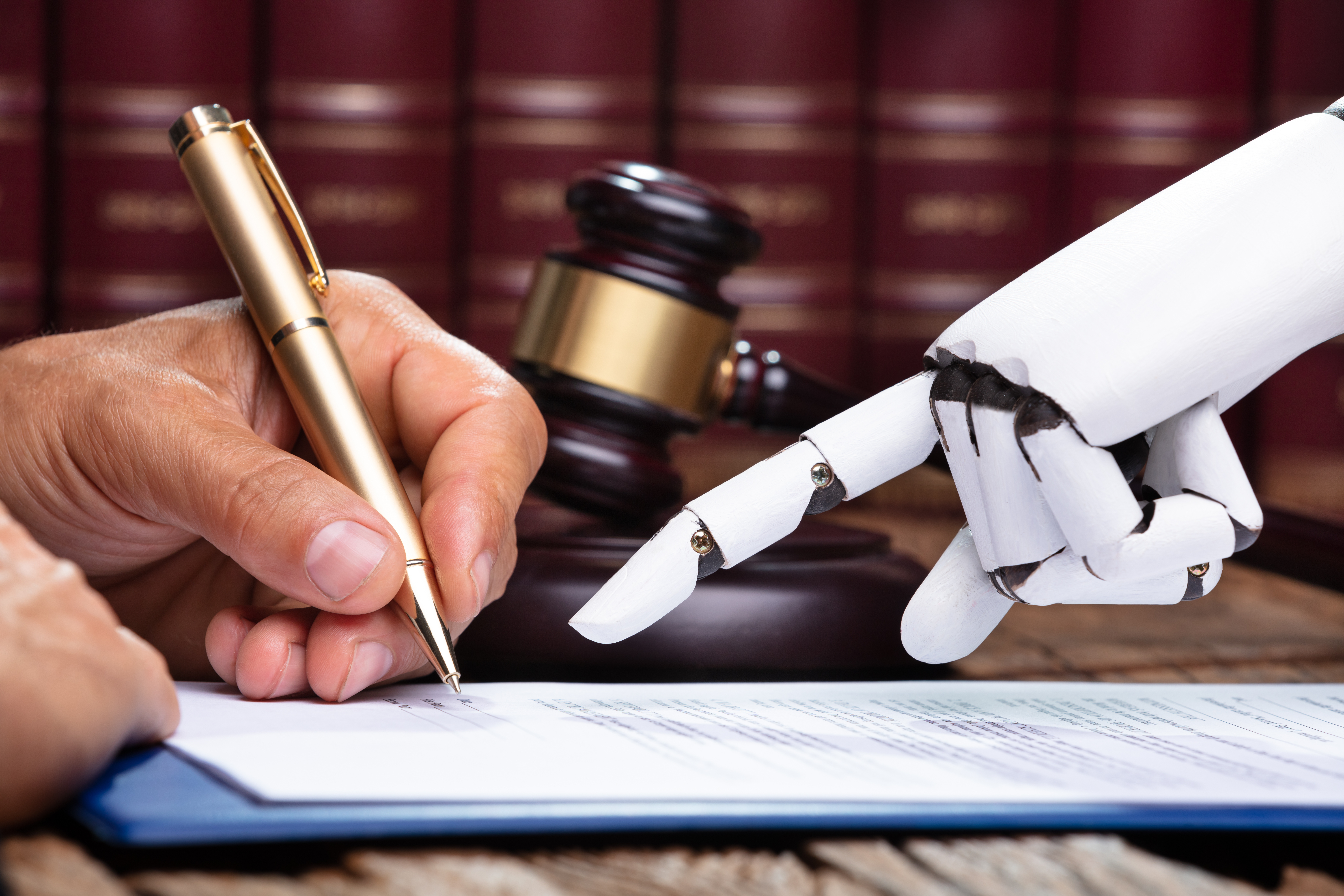 A robot hand helps a human hand sign a law document.