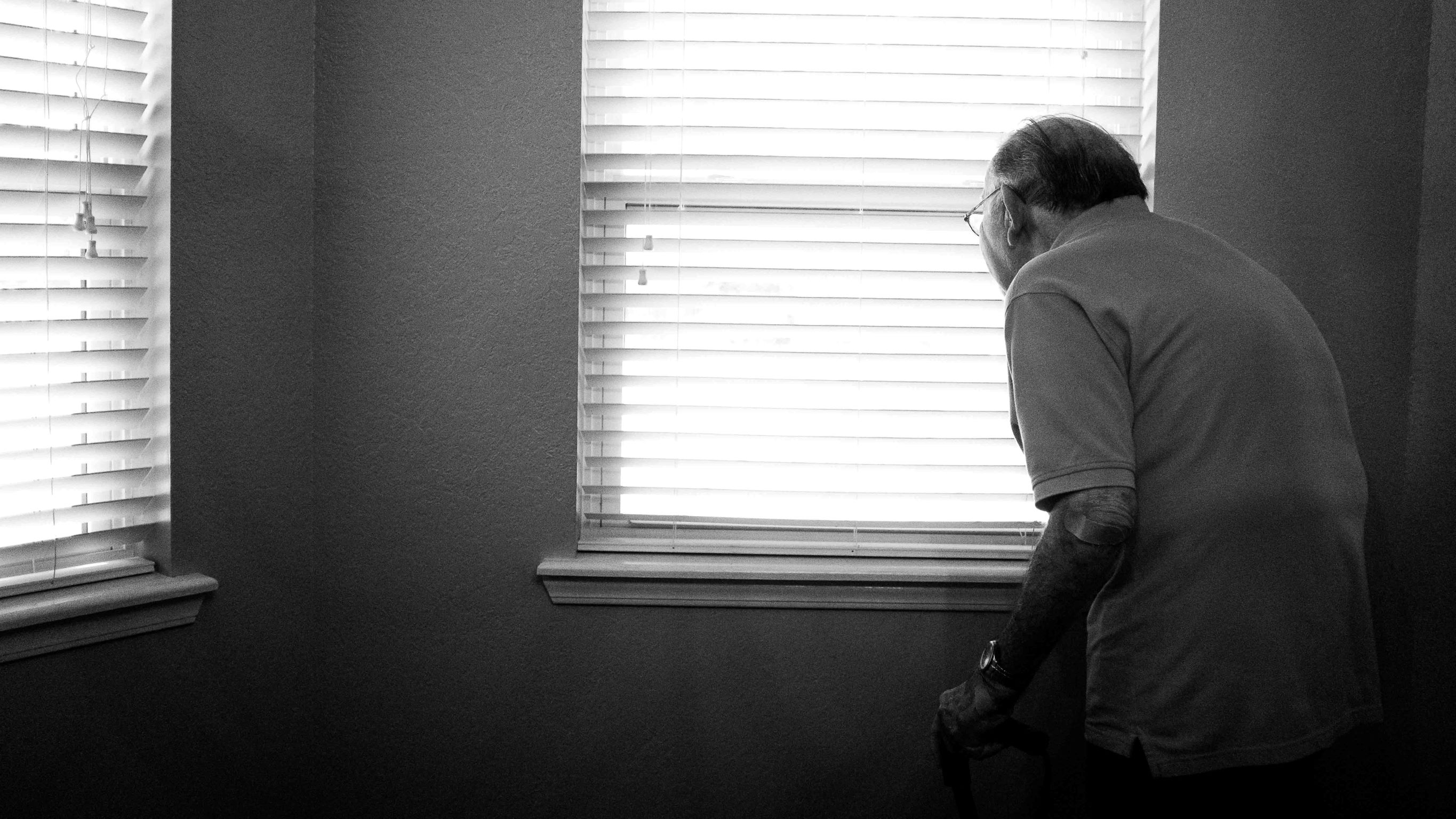 An old man looking out of the blinds.