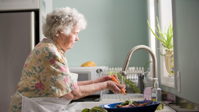 An elderly woman washing vegetables in a sink.