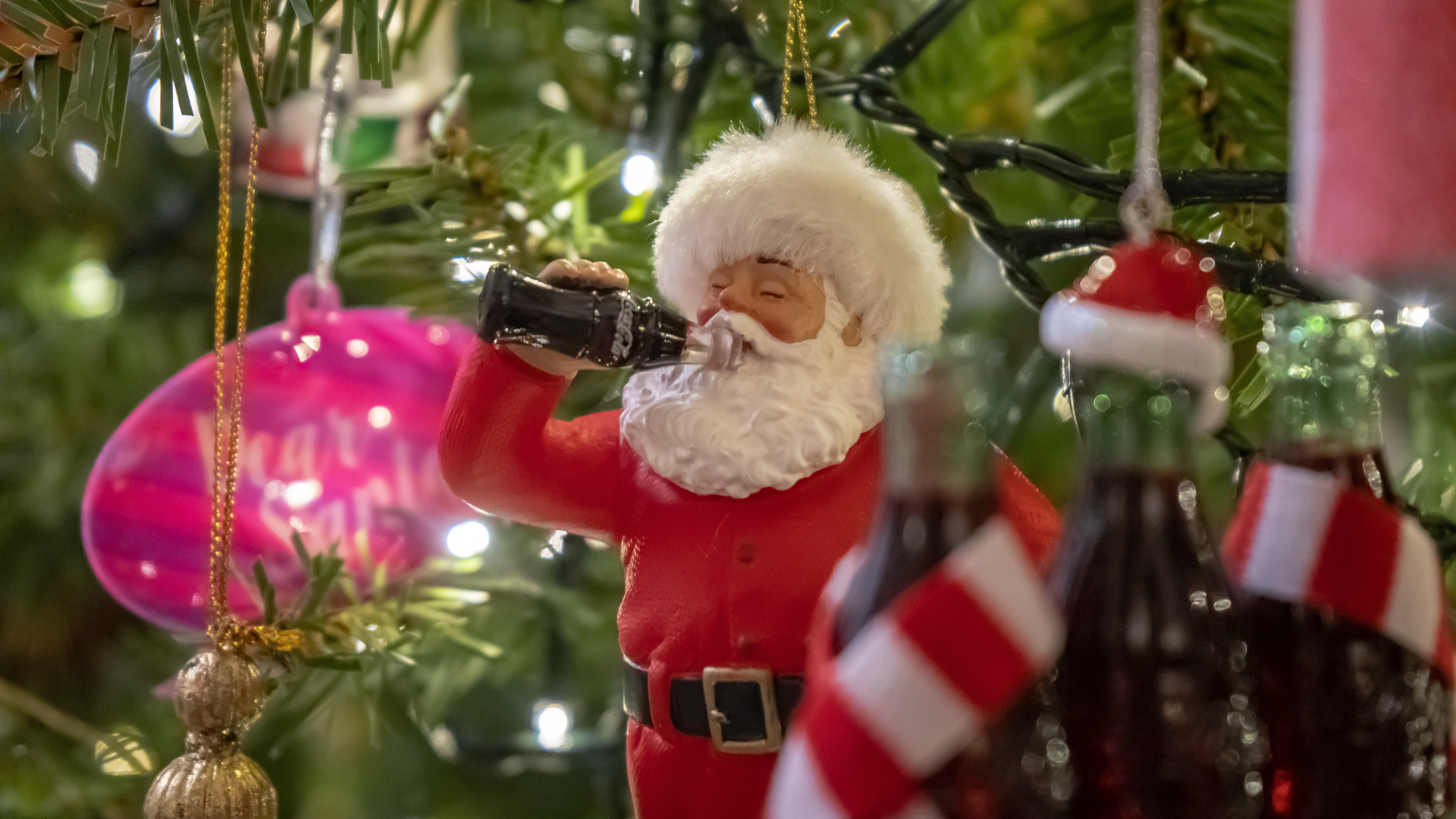 A Santa Claus Christmas tree decoration drinking cola.