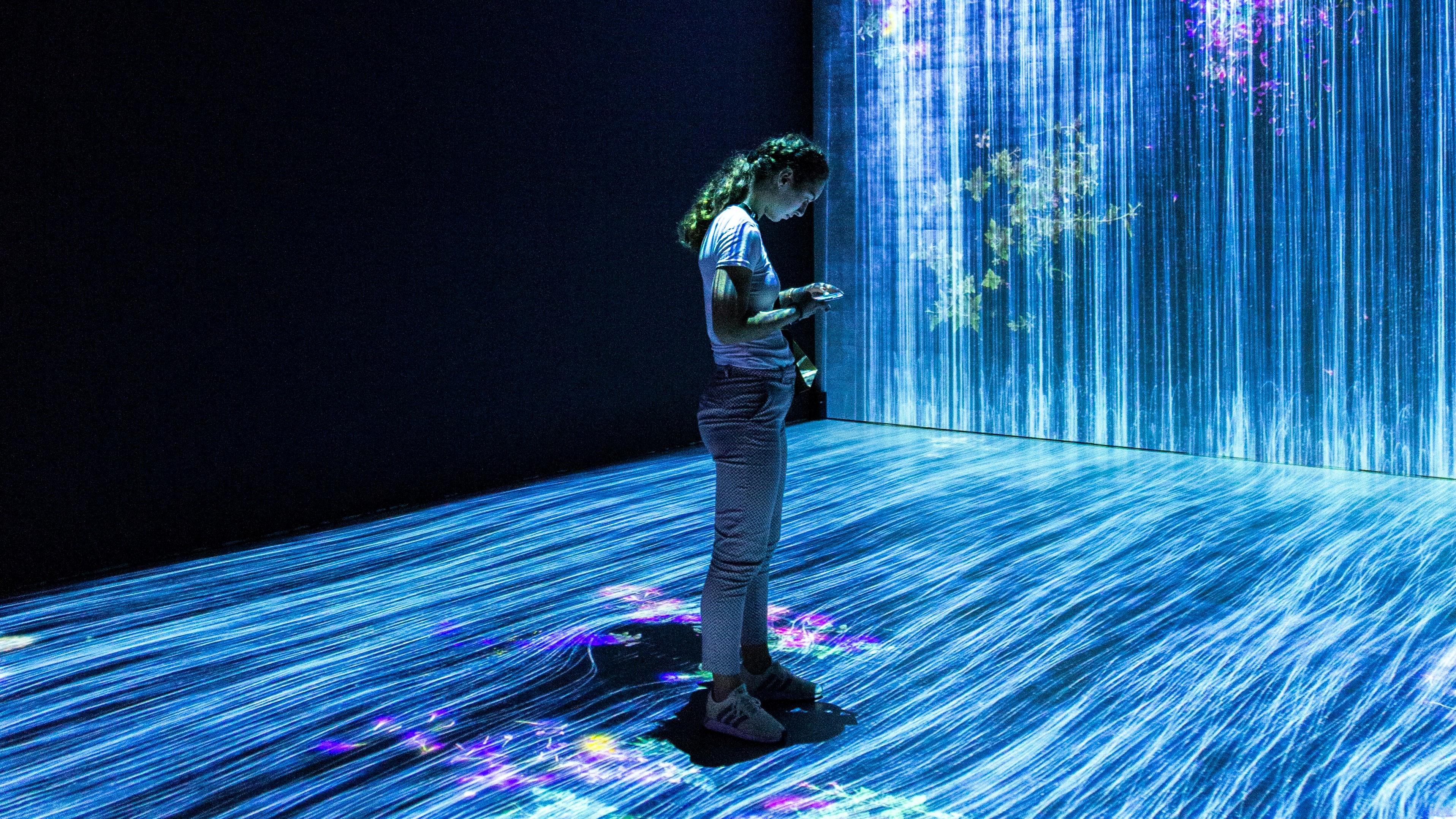 A woman stands looking at her phone in the center of an artistic display of data.
