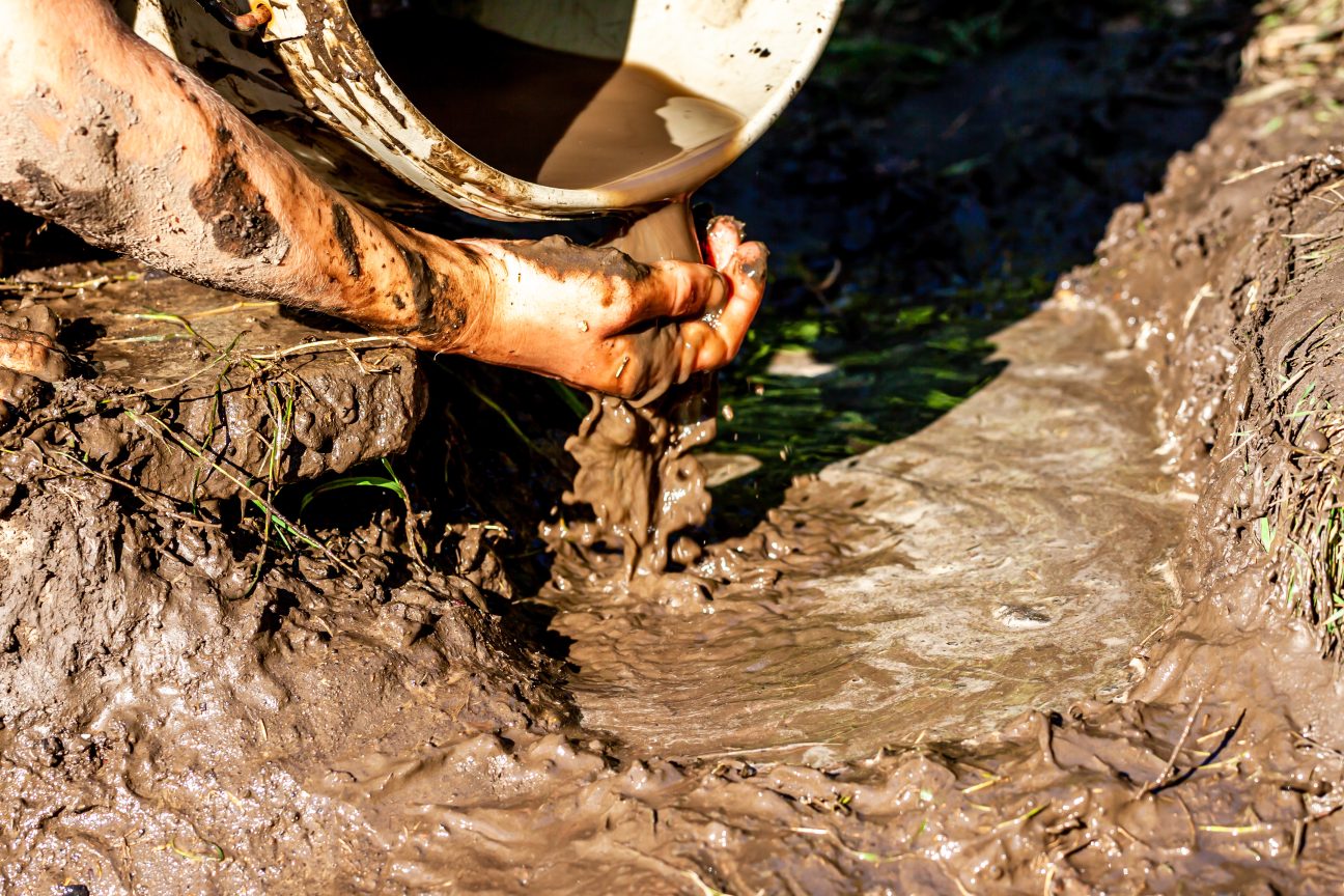 A dirty hand feels muddy sludge as it drains from a pipe.