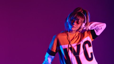 A woman with a music personality wearing earphones and a t-shirt in front of a purple background.