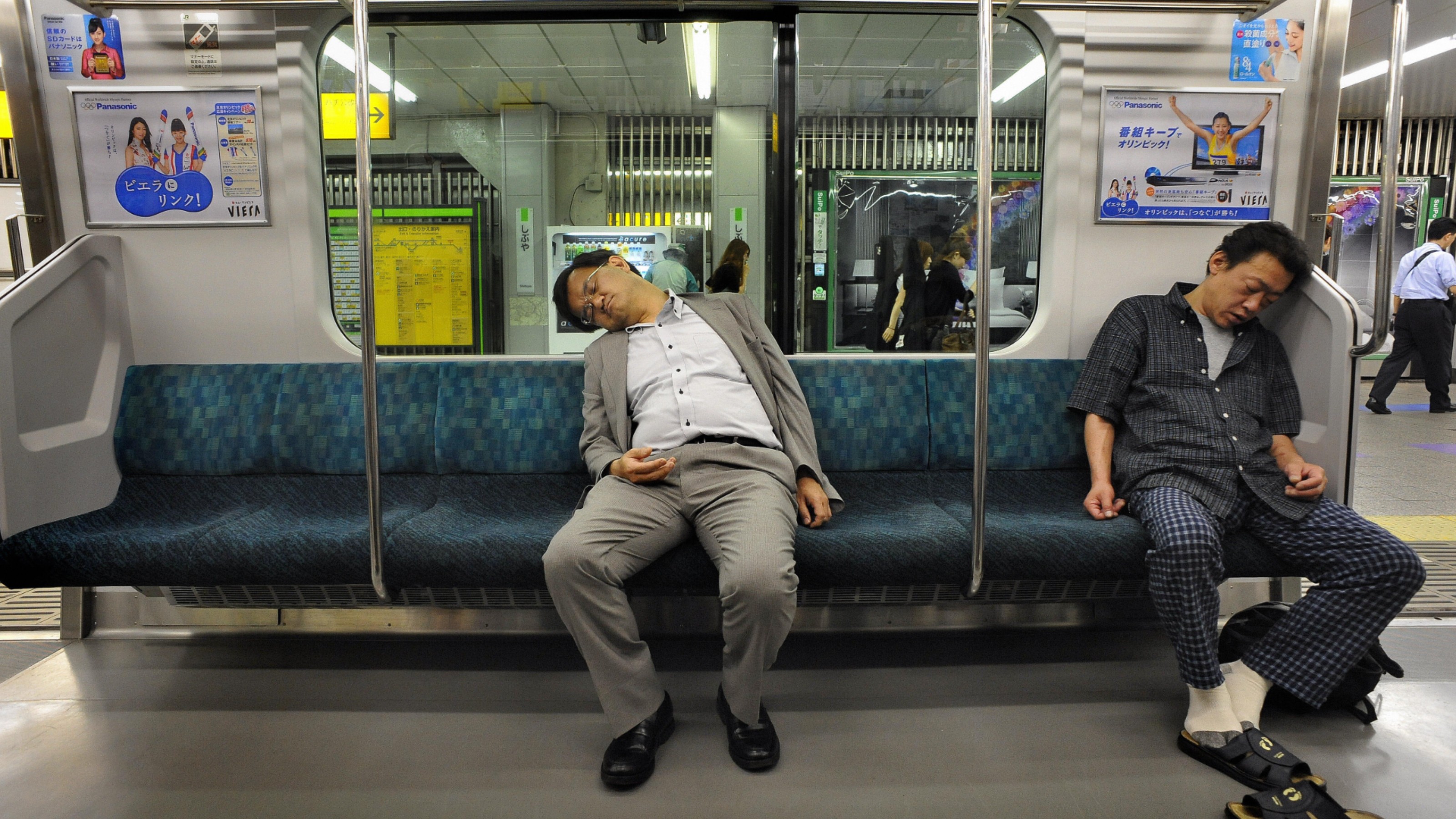 Two Japanese men sleep on a train car.