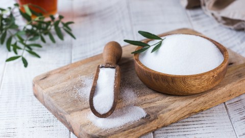 a wooden bowl filled with erythritol next to a wooden spoon.