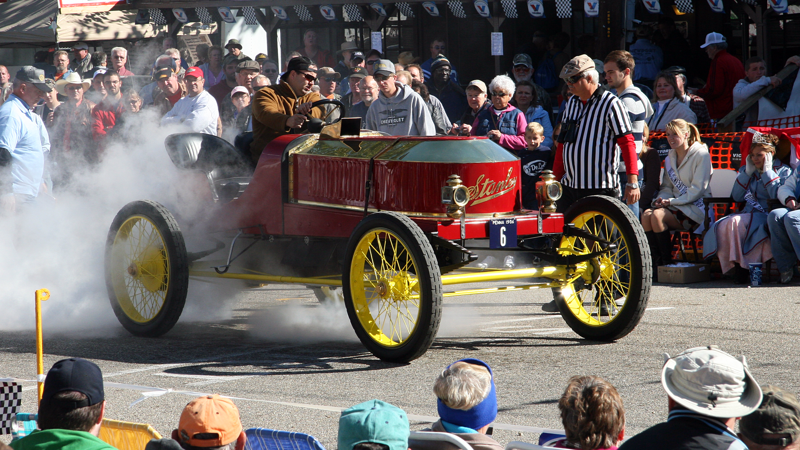 a red and yellow car driving down a street next to a crowd.