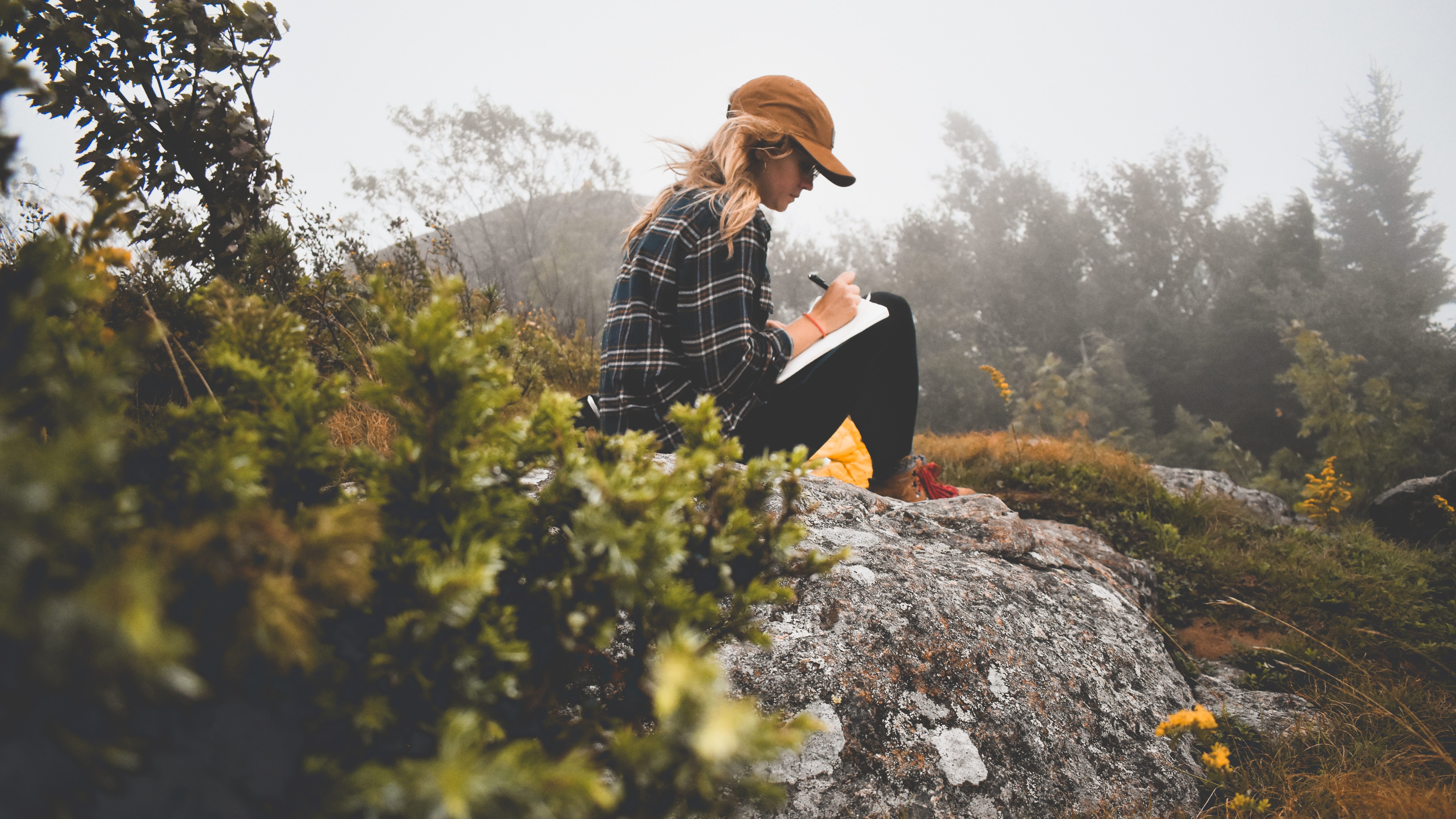 A woman sitting on top of a rock writing in her journal
