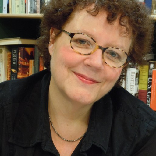 a woman with glasses smiling in front of a bookshelf.