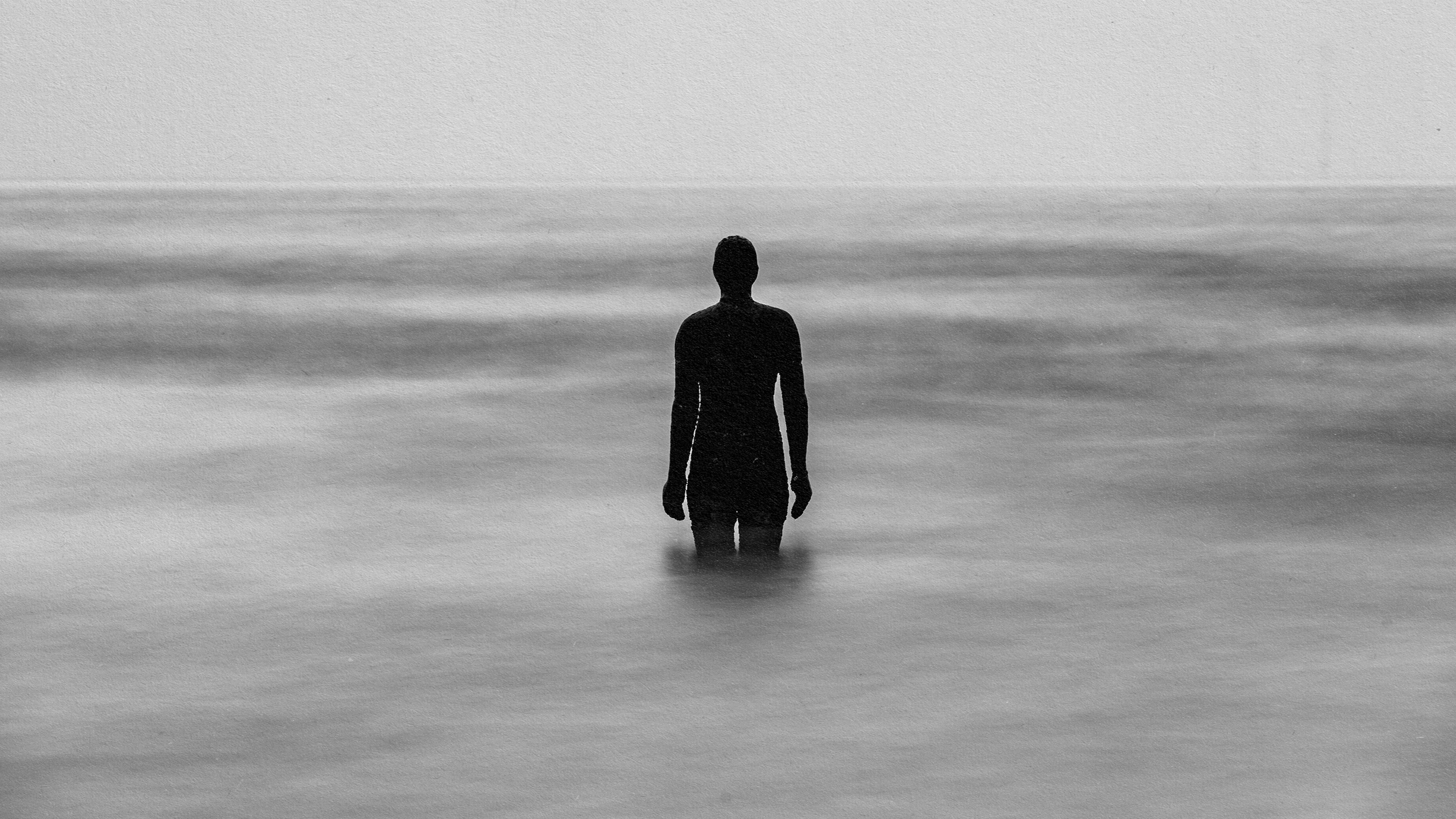 A person standing in the ocean captured in a haunting black and white photo.