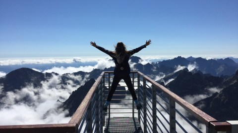 A woman standing on top of a metal railing above a mountain range.