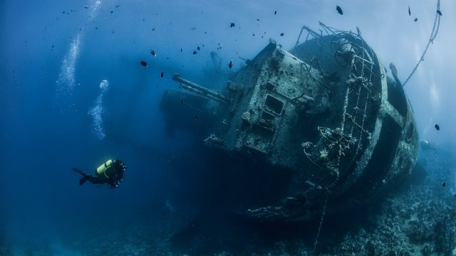 a man scubas near a ship in the ocean.