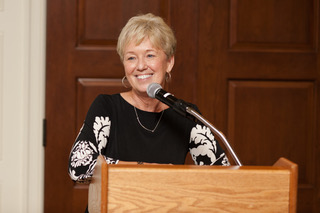 A woman smiles at a podium while giving a speech.