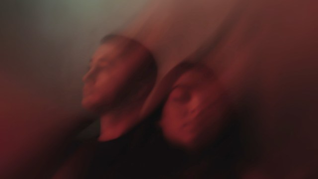 A distorted image of two people in front of a vibrant red background.