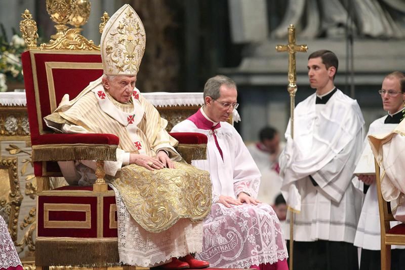 Pope Benedict XVI sits on a throne in front of a group of priests.