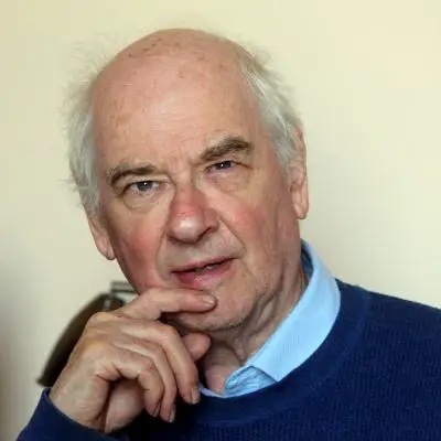an older man in a blue sweater with his hand on his chin.