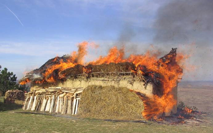 A burning house in a field.