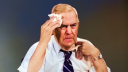 A man in a tie is holding a tissue to his face.