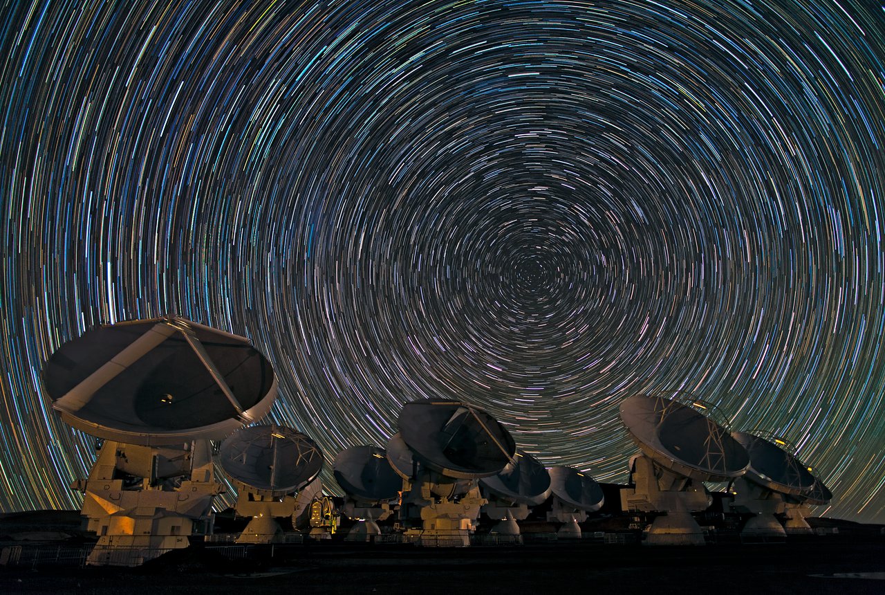 A group of telescopes with star trails in the sky.