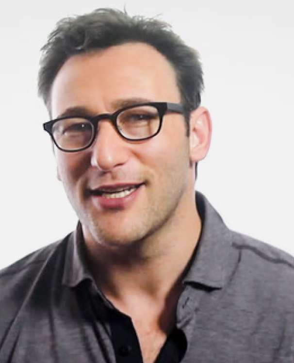 Simon Sinek smiling in front of a white background.