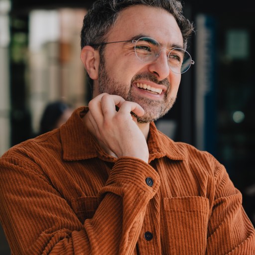 A smiling man wearing glasses and an orange shirt.