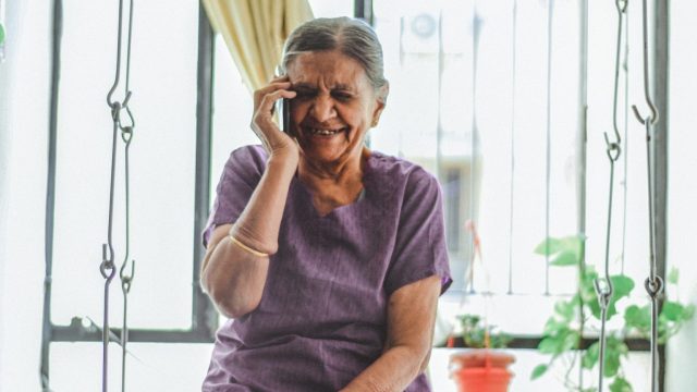 An elderly woman sitting on a chair and talking on the phone.