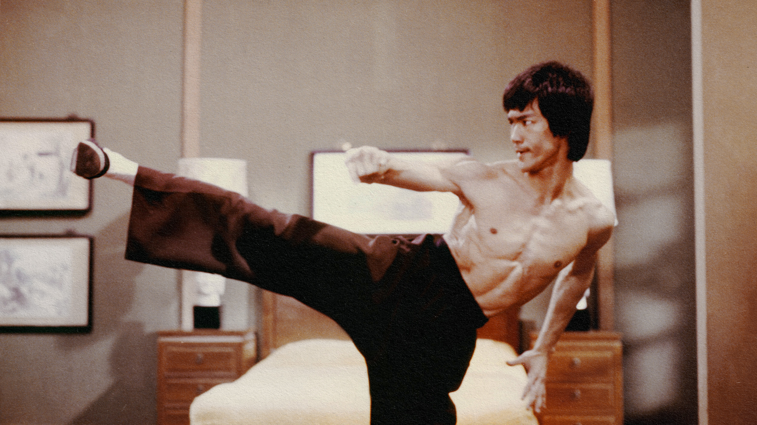 Bruce Lee executing a pain-free kick in a bedroom.
