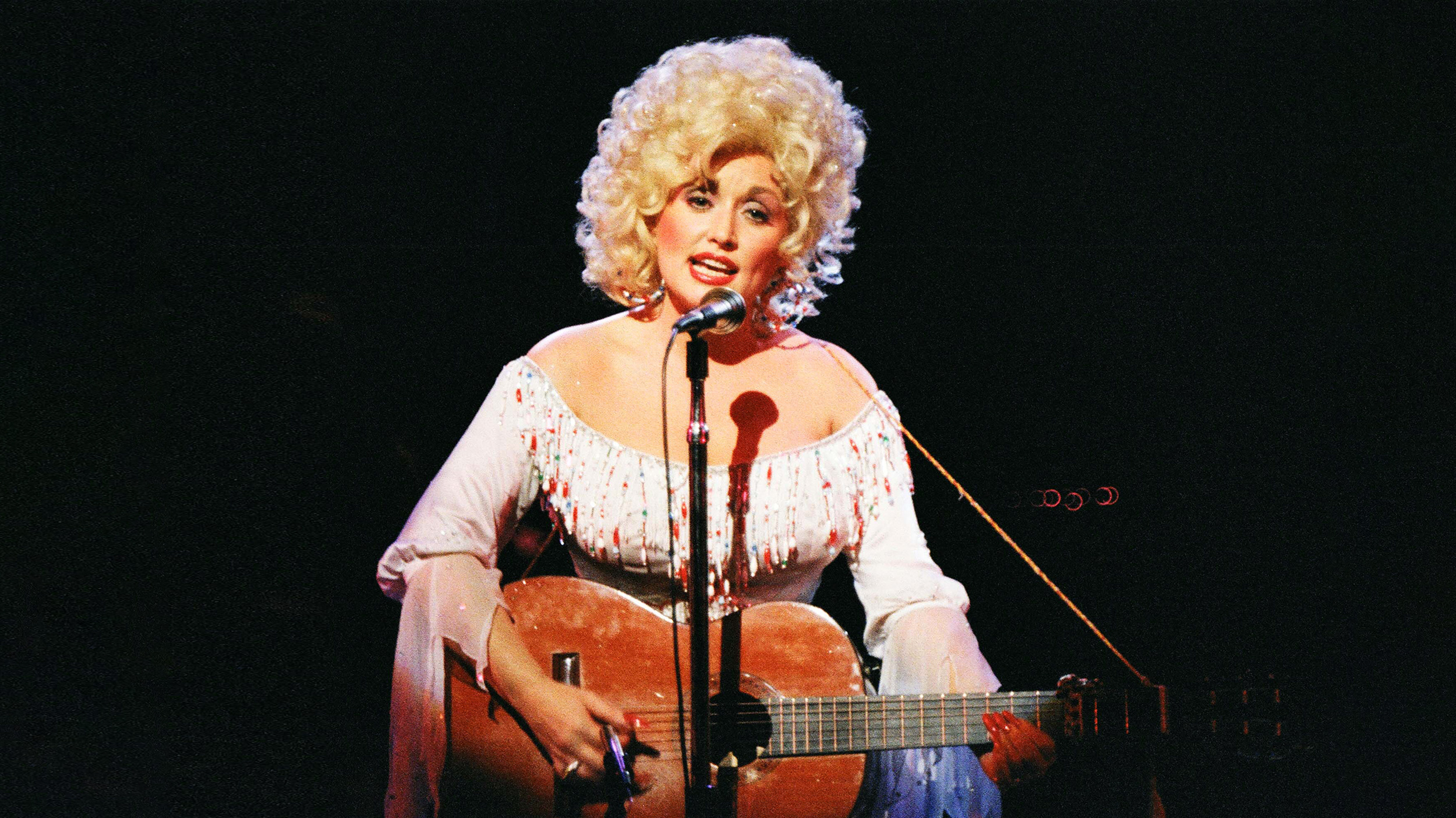 Dolly Parton on stage with an acoustic guitar showcases her musical talent.