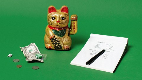 A Chinese lucky cat figurine with a kakeibo notepad on a green background.