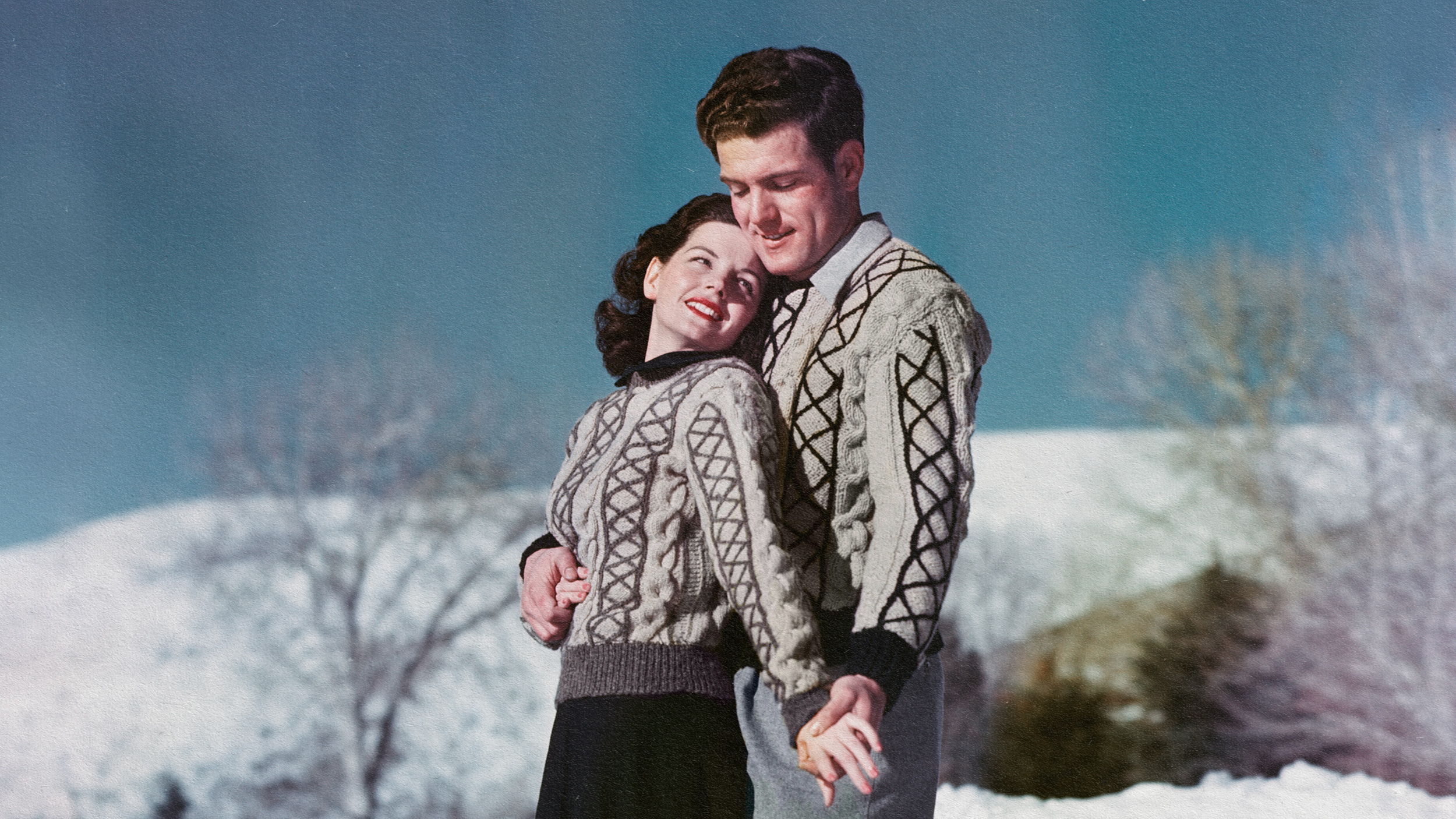 A man and woman wearing sweaters standing in the snow, showcasing how opposites attract.