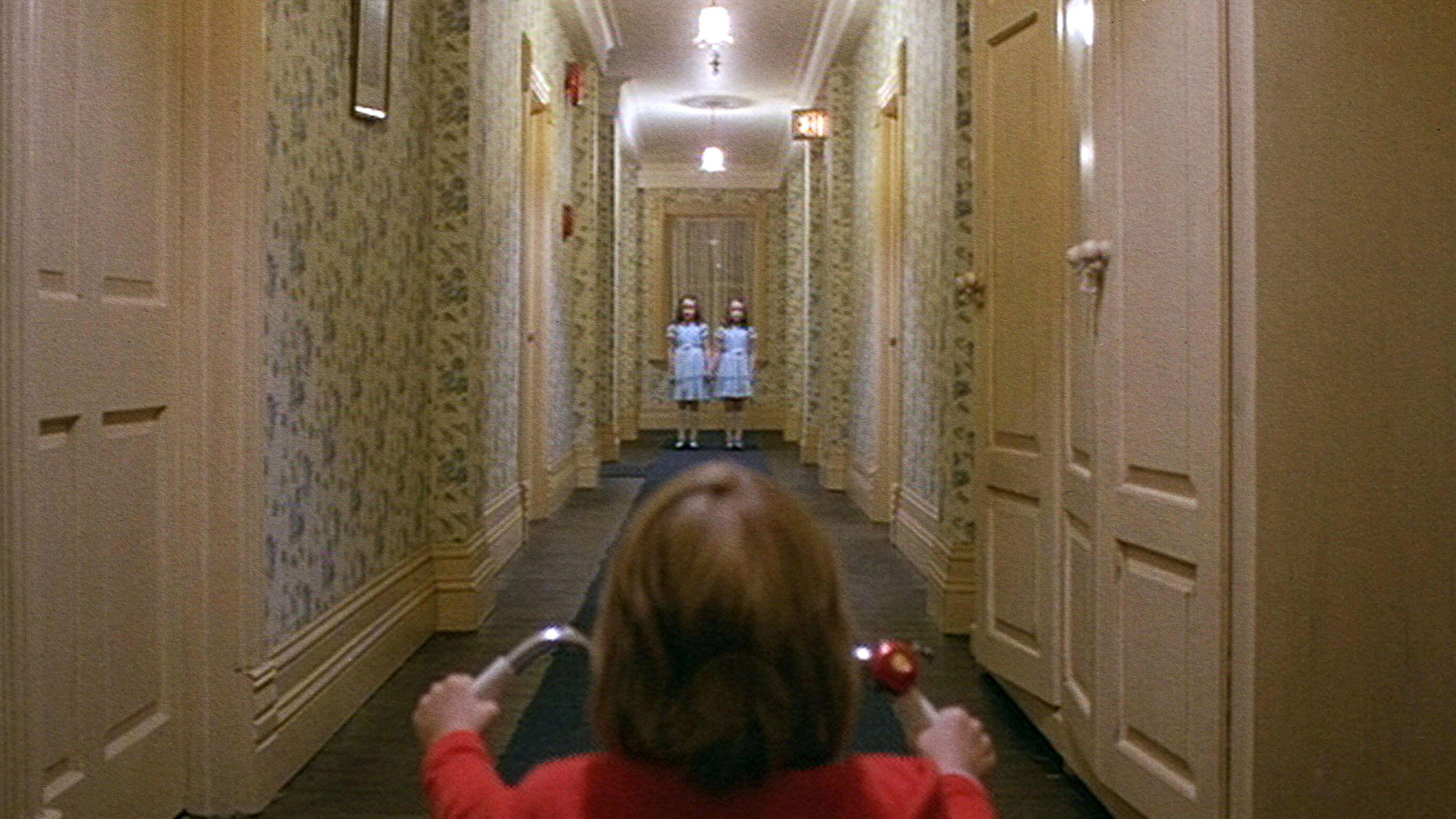 A girl is walking down a hallway in a red shirt, feeling fear.