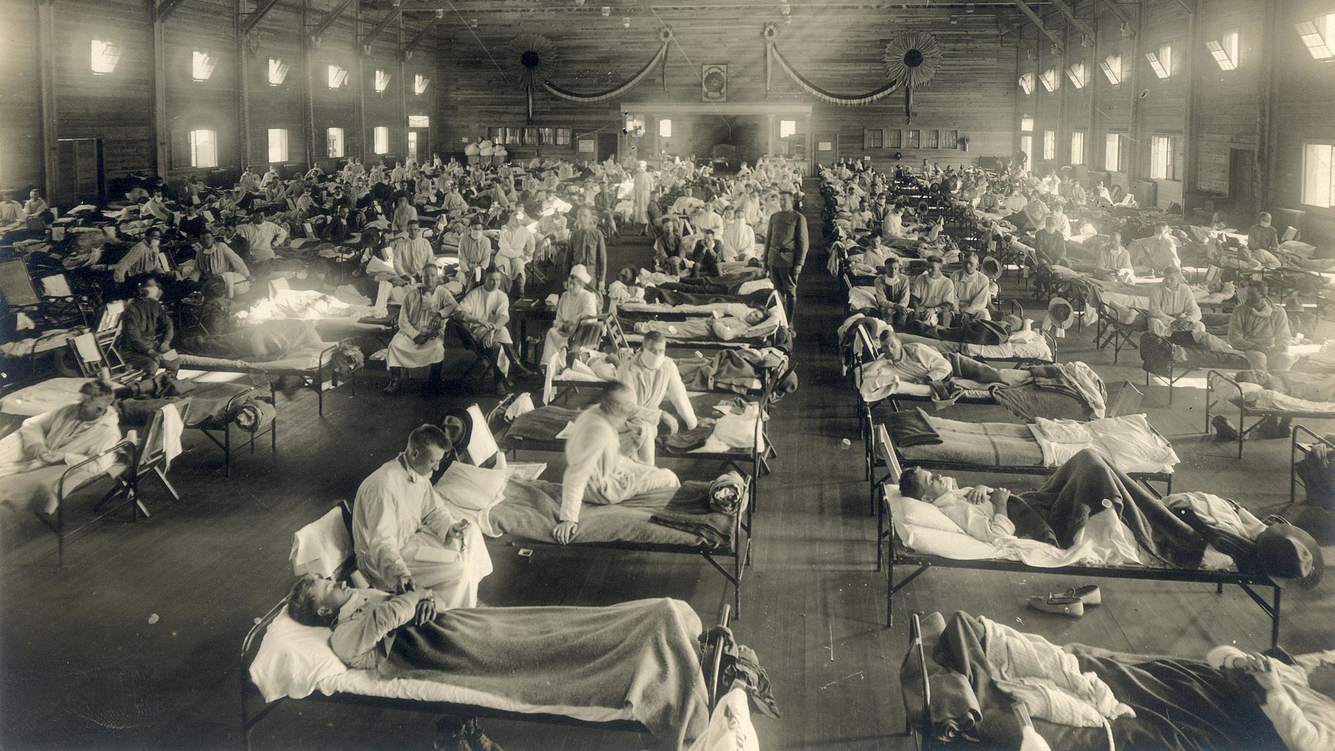 During the 1918 flu pandemic, a group of individuals lay together on beds in a vast room, seeking solace and care.