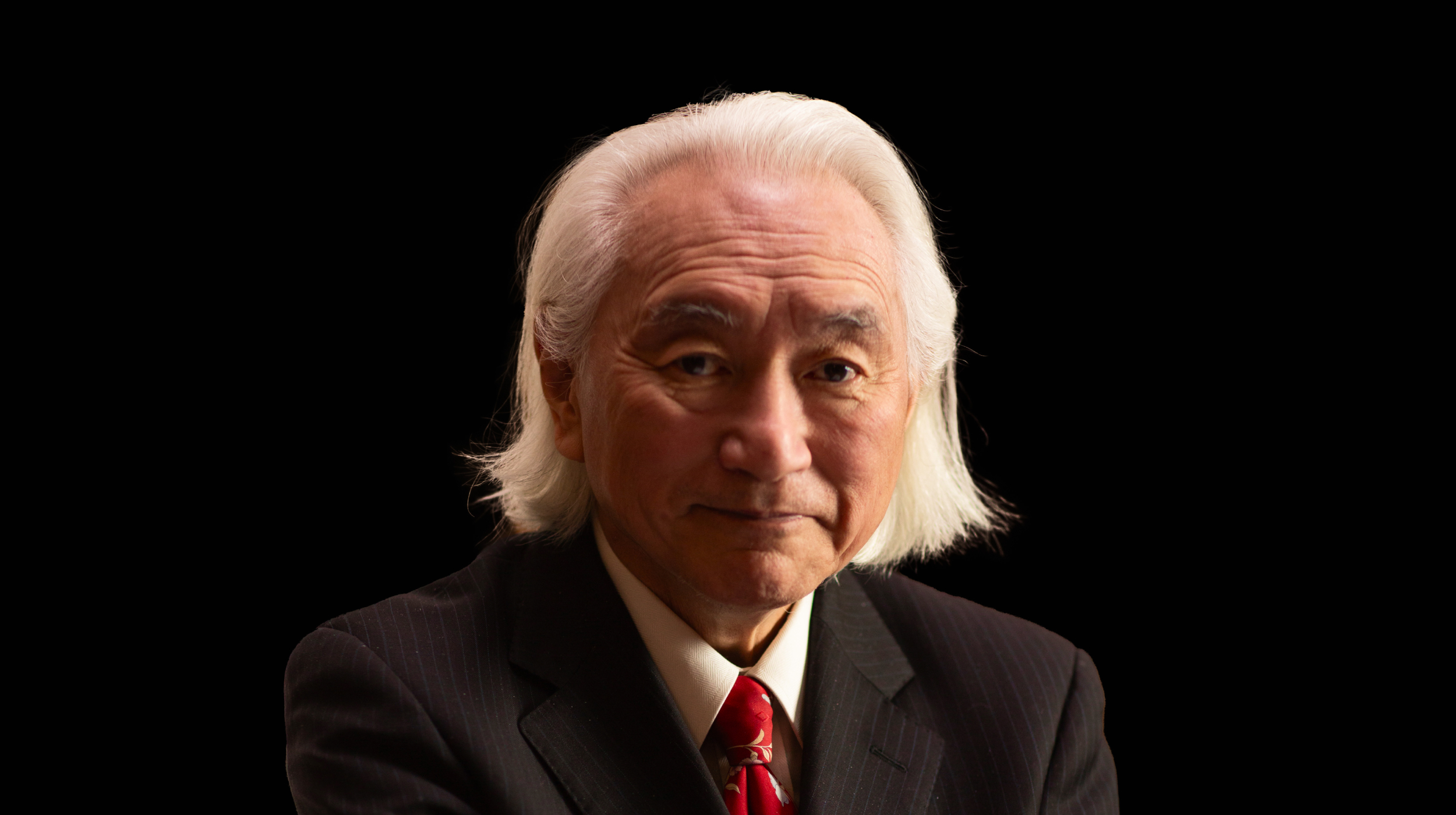 A man in a suit with white hair and a red tie.