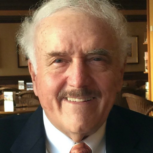 An older man in a suit and tie smiles for the camera.