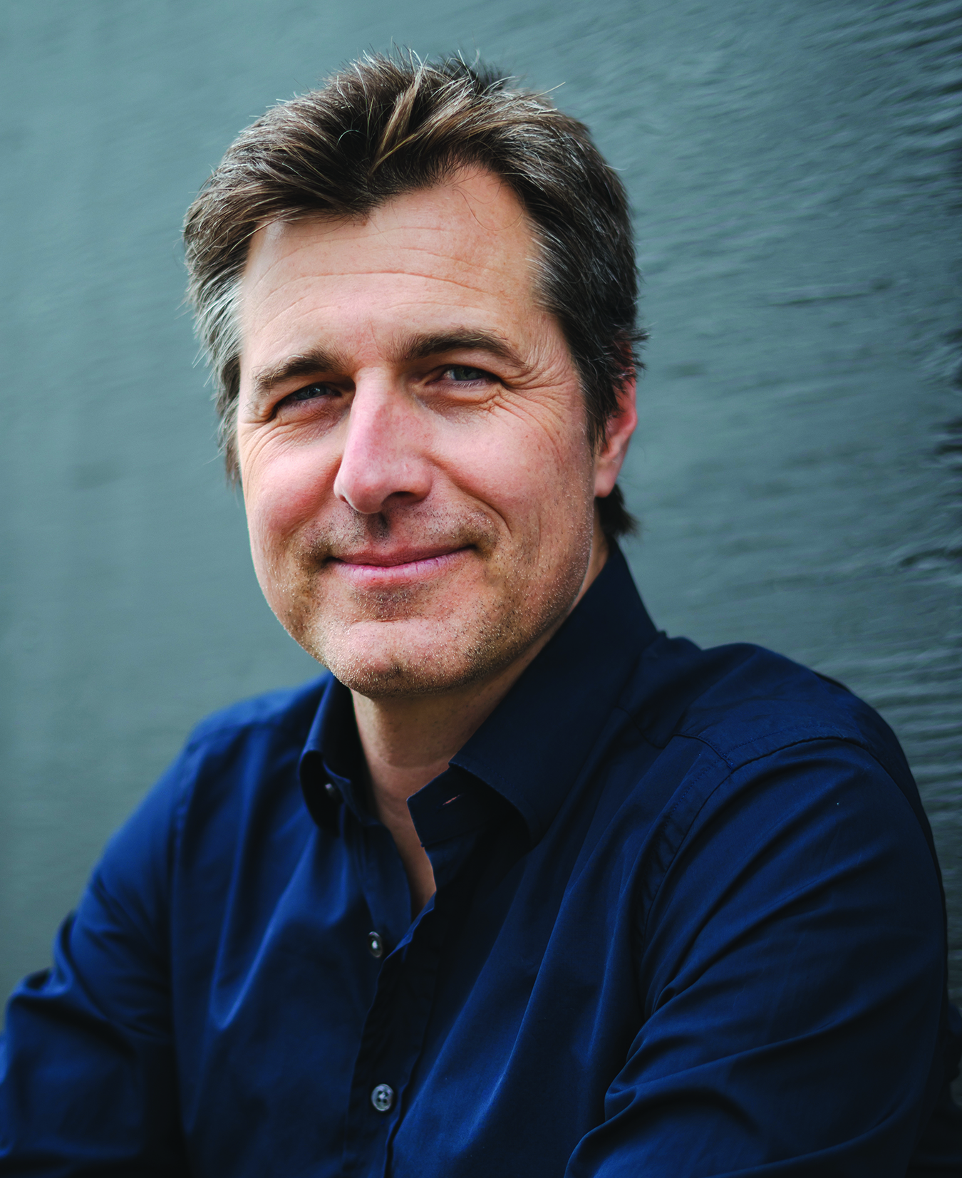A man in a blue shirt leaning against a wall.