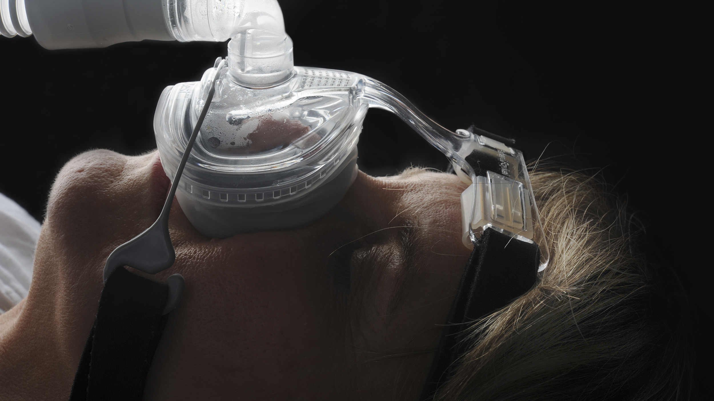A woman wearing a sleep apnea mask with a bottle of water.