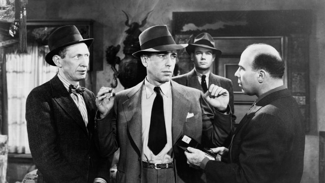 Three men in suits and hats talking to each other, uncovering plot holes.