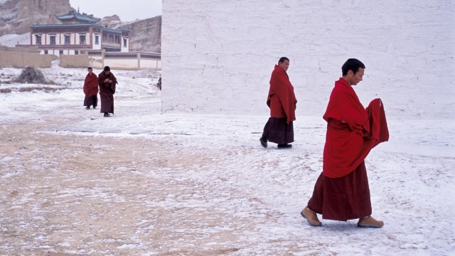 Monks in red robes walking in the snow during biostasis.