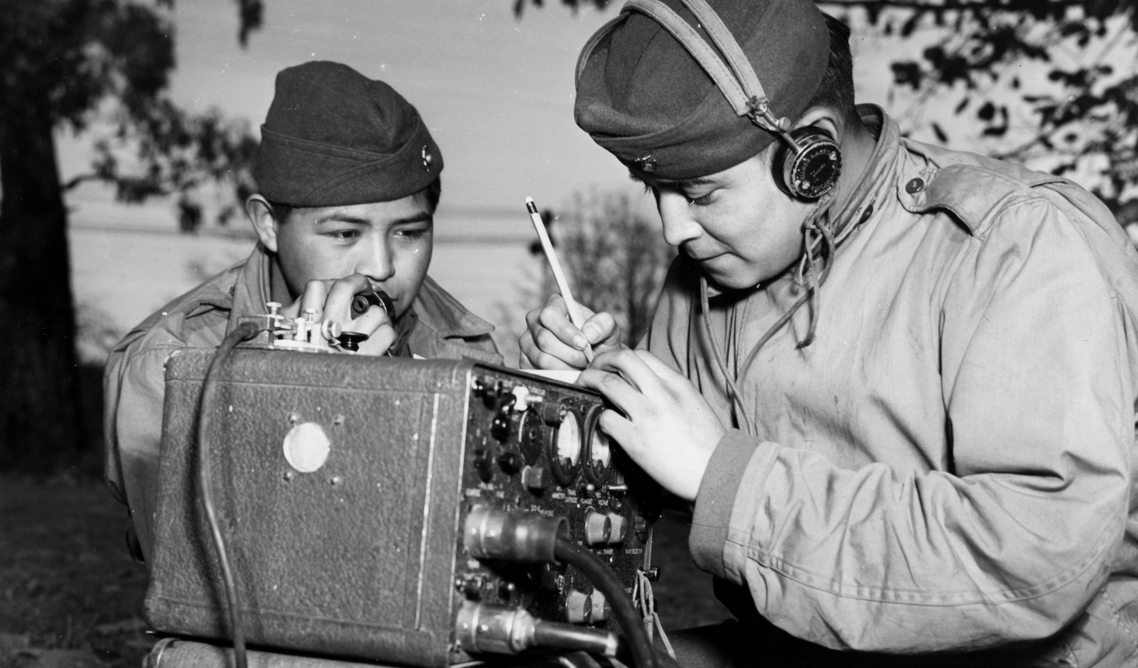 Two navajo men in military uniforms working on a radio.