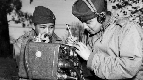 Two navajo men in military uniforms working on a radio.