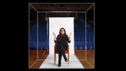An image of a woman sitting in a chair in front of an auditorium.