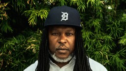 A man with dreadlocks standing in front of a bush.