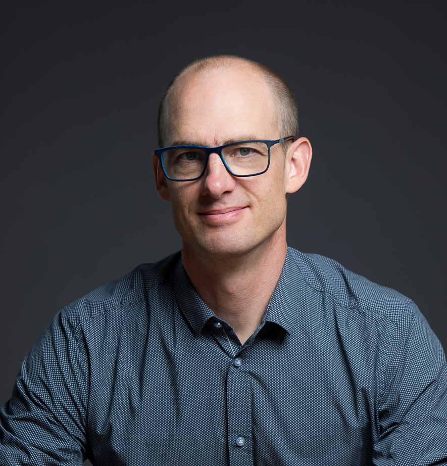 A bald man wearing glasses and a blue shirt.
