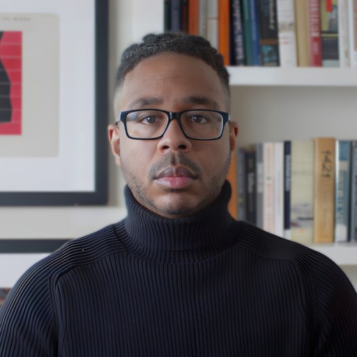 A man wearing glasses and a turtleneck sweater in front of a bookshelf.