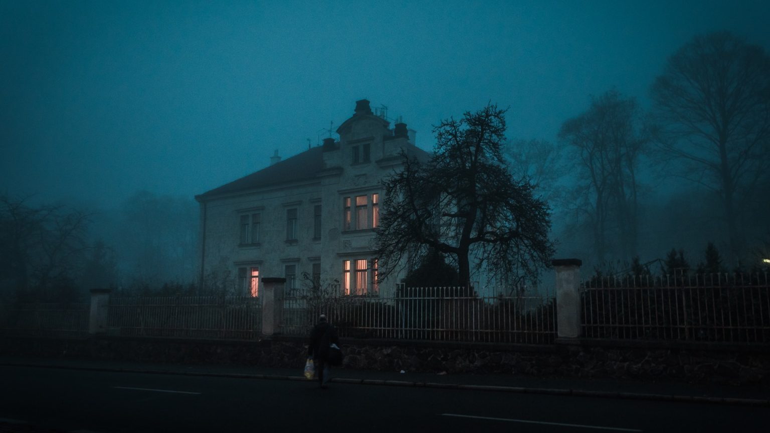 A person walks past a house in the fog.