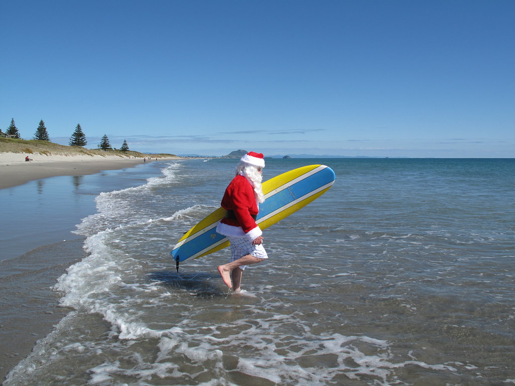 A hazard santa claus walking with a surfboard.
