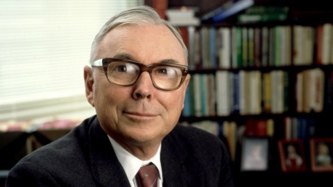 Charles Munger, a man in glasses, sitting in front of a bookcase filled with puzzles.