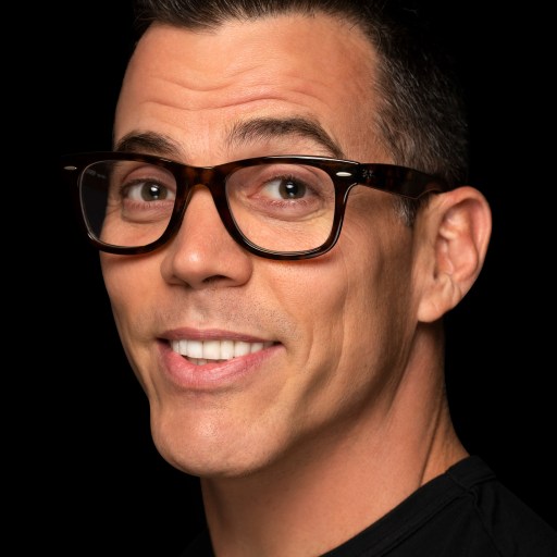 A man in glasses smiling in front of a black background.